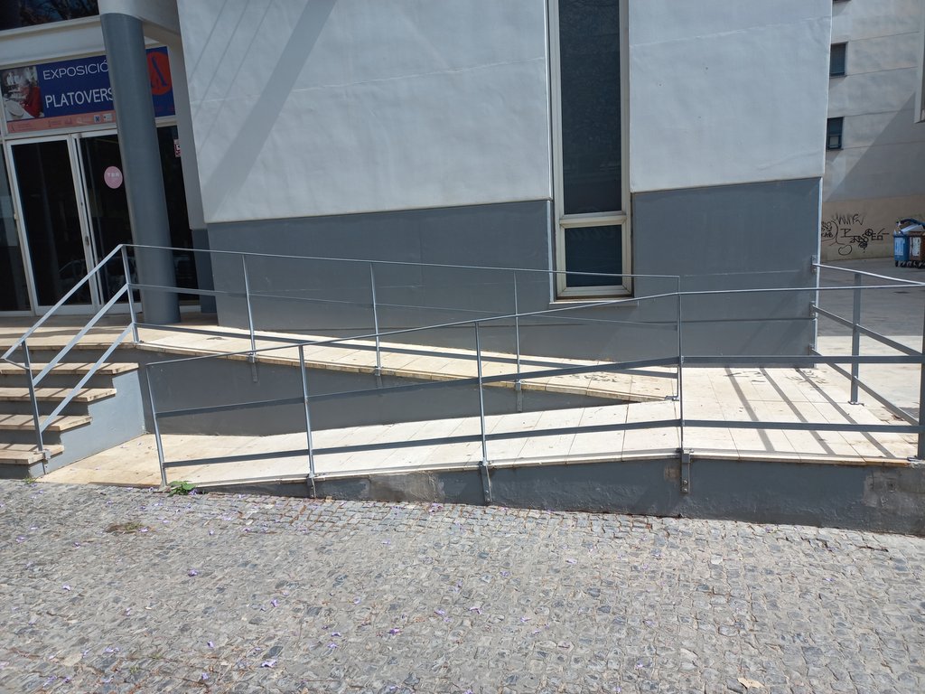 Desnivel resuelto mediante rampa practicable (pendiente, meseta, pasamanos y barandilla).