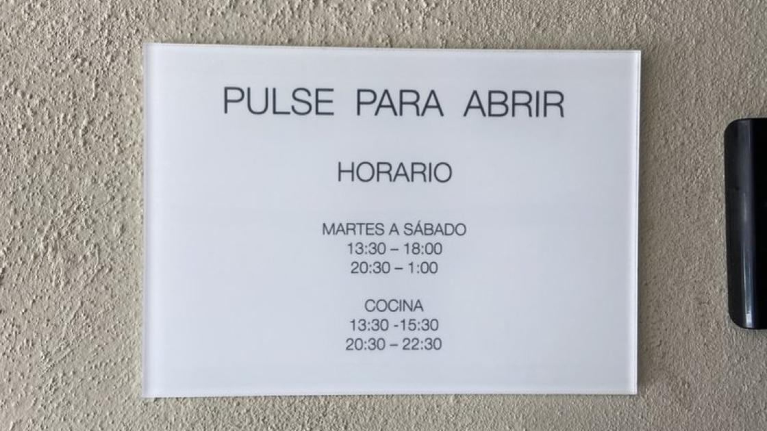 Signage for the door opener button and opening hours at the main entrance.