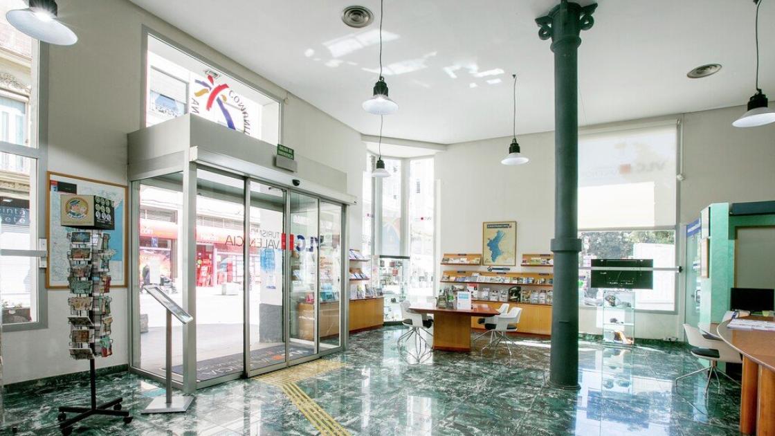 Interior de l'oficina de turisme amb espai de descans i senyalització al terra.