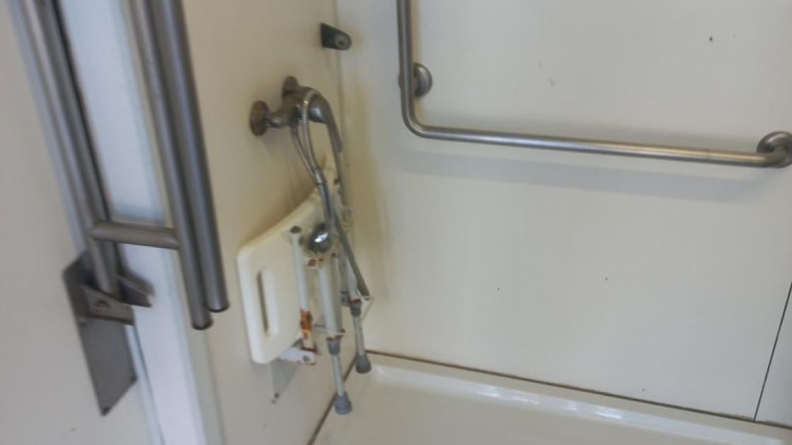 Baño adaptado equipado de ducha accesible con asiento abatible y barras de sujeción.